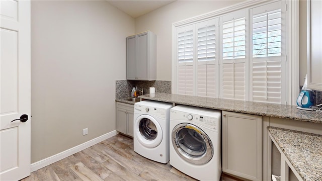 washroom with light wood-style flooring, a sink, washing machine and dryer, cabinet space, and baseboards