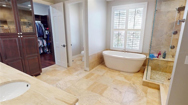 bathroom featuring a freestanding tub, a sink, a shower stall, a walk in closet, and toilet