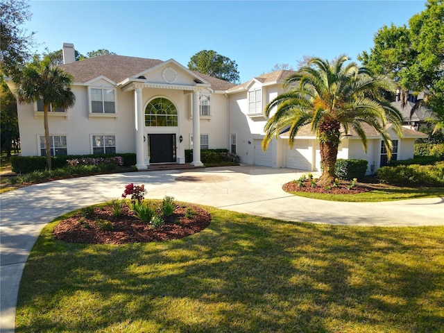 view of front of property with stucco siding, a front lawn, a chimney, and driveway