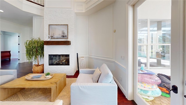 living room with wood finished floors, baseboards, a large fireplace, and ornamental molding