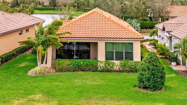 rear view of house featuring stucco siding, a tile roof, a yard, and a water view