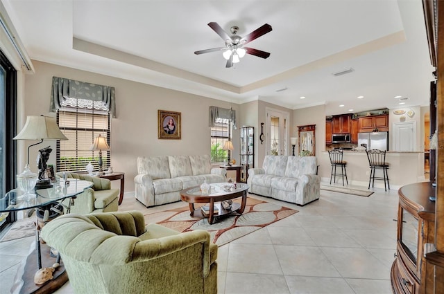 living area with a tray ceiling, visible vents, and a healthy amount of sunlight