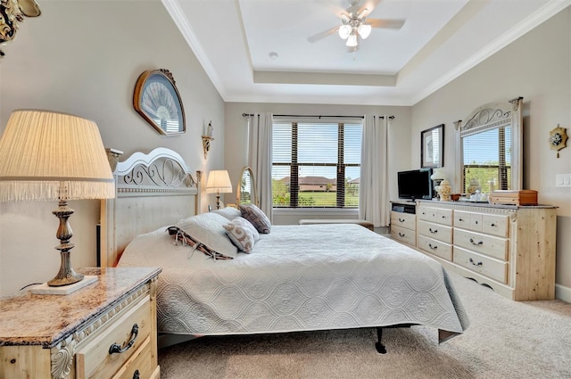 carpeted bedroom with a tray ceiling, crown molding, and ceiling fan