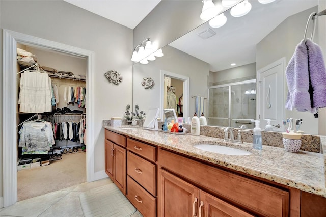 bathroom with a walk in closet, visible vents, a stall shower, a sink, and double vanity