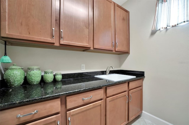 kitchen with light tile patterned floors, dark stone countertops, baseboards, and a sink