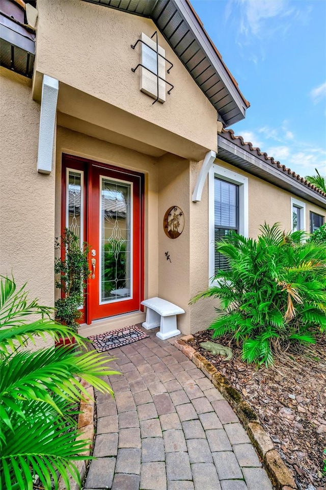 view of exterior entry with stucco siding and a tile roof