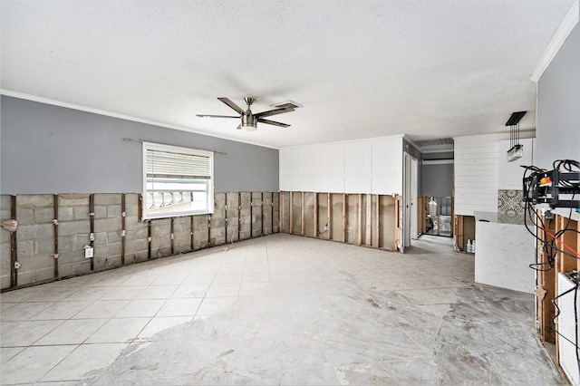 empty room with ceiling fan, a textured ceiling, a wainscoted wall, and ornamental molding