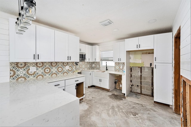 kitchen featuring visible vents, a sink, stainless steel microwave, white cabinetry, and light stone countertops