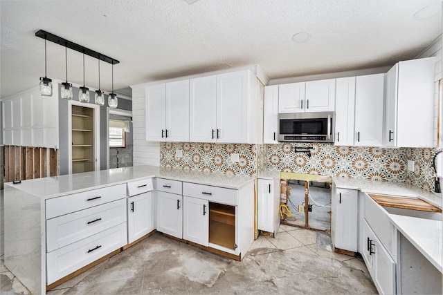 kitchen with stainless steel microwave, tasteful backsplash, a peninsula, white cabinets, and light countertops