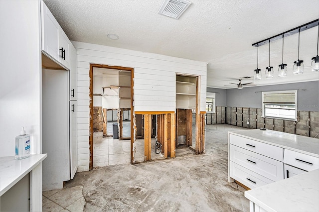 kitchen with visible vents, a textured ceiling, white cabinets, and a ceiling fan