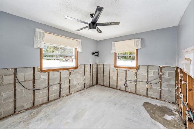 interior space featuring concrete block wall, a textured ceiling, unfinished concrete flooring, and ceiling fan