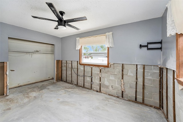 unfurnished bedroom featuring concrete floors, ceiling fan, a closet, a textured ceiling, and concrete block wall