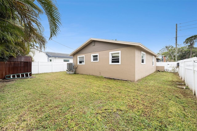 back of house featuring a yard, a fenced backyard, central AC, and stucco siding