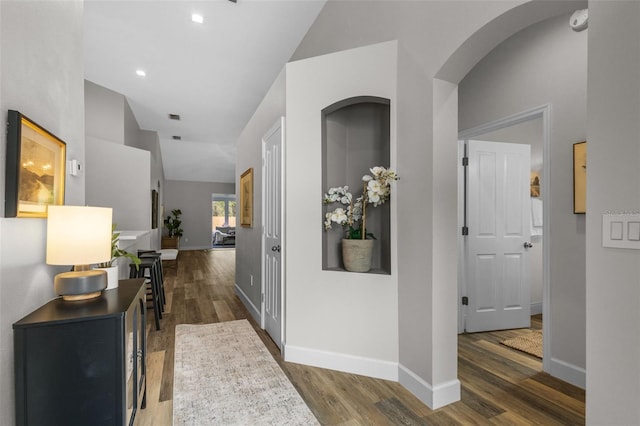 hallway featuring baseboards, wood finished floors, and vaulted ceiling