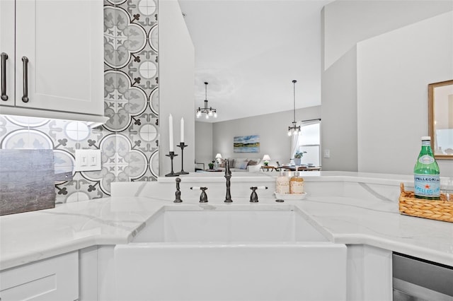 kitchen featuring a sink, light stone countertops, a notable chandelier, and white cabinetry