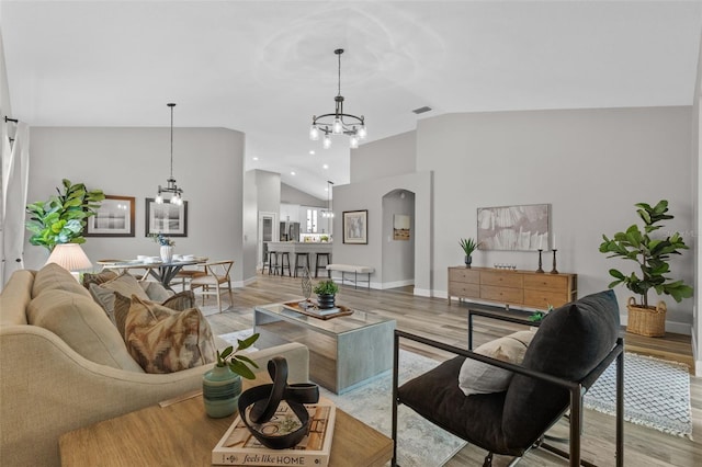 living area with visible vents, baseboards, light wood-style floors, a notable chandelier, and high vaulted ceiling