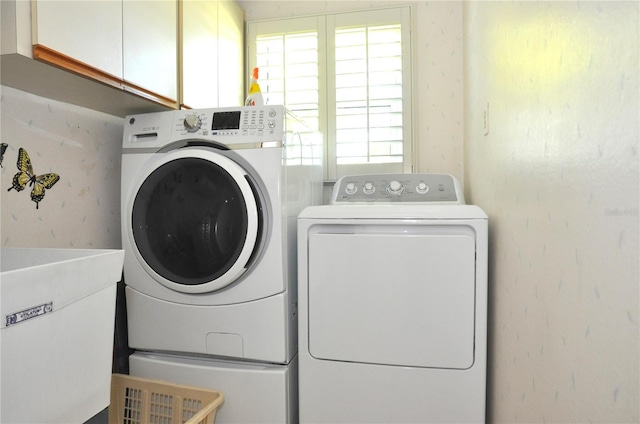 laundry area with wallpapered walls, cabinet space, independent washer and dryer, and a sink