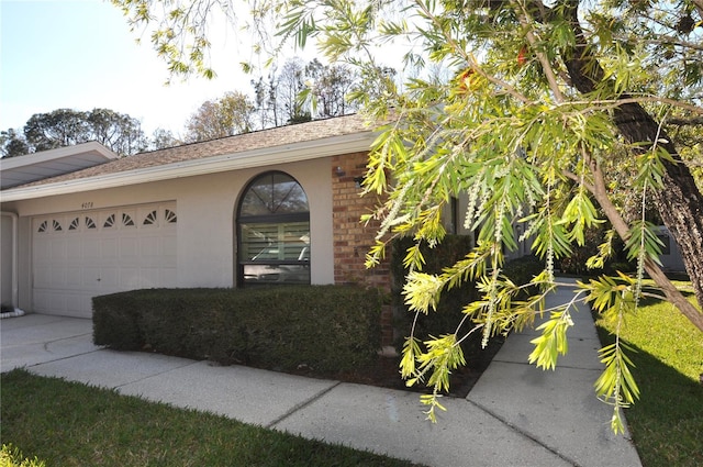 exterior space with concrete driveway, an attached garage, brick siding, and stucco siding