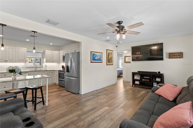 living area featuring visible vents, baseboards, light wood-style flooring, and a ceiling fan