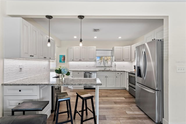 kitchen featuring visible vents, a sink, appliances with stainless steel finishes, a kitchen bar, and light wood-type flooring