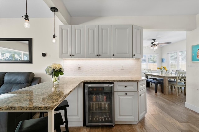 kitchen featuring light stone counters, wood finished floors, wine cooler, white cabinets, and backsplash