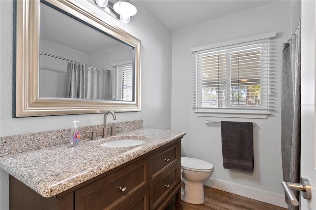 bathroom with vanity, toilet, wood finished floors, and baseboards