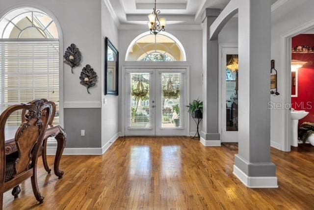 foyer entrance featuring baseboards, a tray ceiling, french doors, wood finished floors, and arched walkways