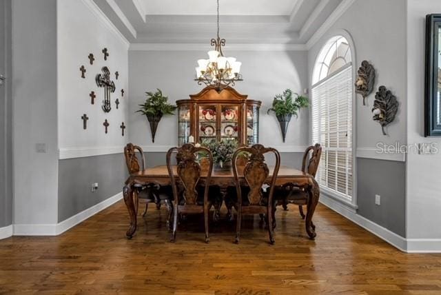 dining space featuring wood finished floors, a raised ceiling, a chandelier, and ornamental molding