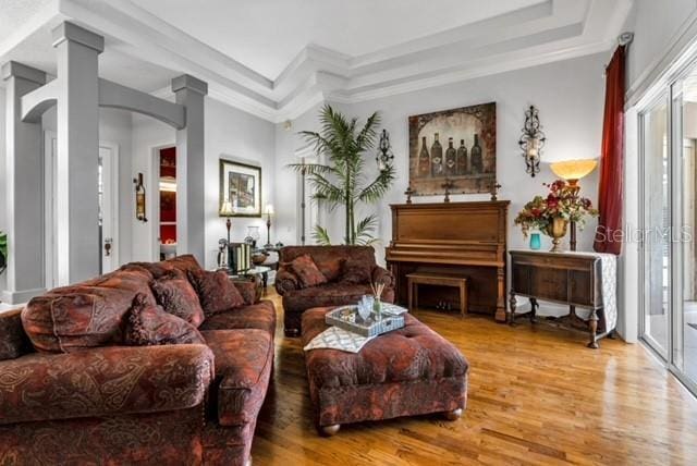 living area with crown molding, a raised ceiling, decorative columns, and wood finished floors