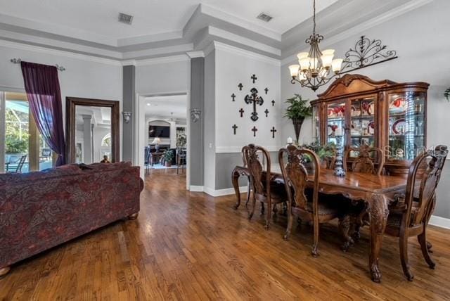 dining space featuring a tray ceiling, visible vents, an inviting chandelier, and wood finished floors