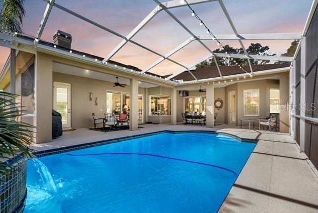 view of pool featuring glass enclosure, a patio, a ceiling fan, and a pool with connected hot tub