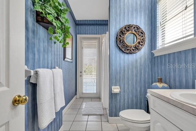 half bath featuring tile patterned flooring, plenty of natural light, toilet, and wallpapered walls