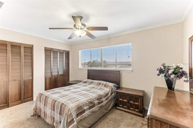 bedroom featuring light colored carpet, a ceiling fan, multiple closets, and ornamental molding