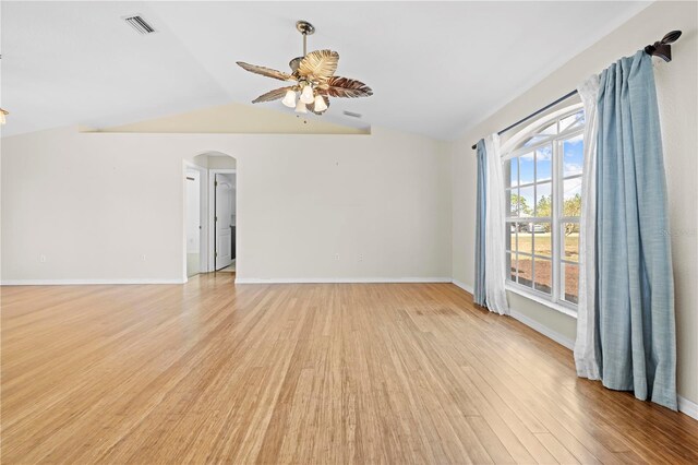 empty room with baseboards, lofted ceiling, arched walkways, ceiling fan, and light wood-type flooring