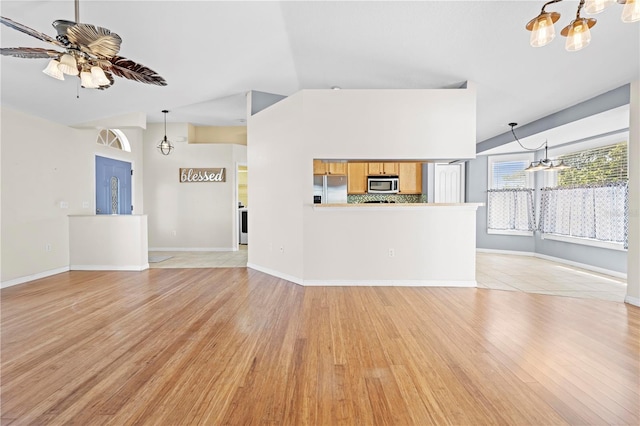 unfurnished living room featuring ceiling fan with notable chandelier, lofted ceiling, light wood-style floors, and baseboards