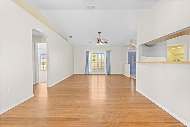 unfurnished living room featuring lofted ceiling, a ceiling fan, arched walkways, and light wood finished floors