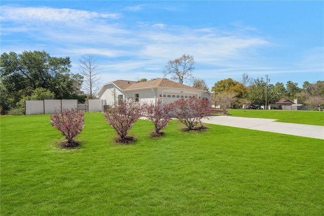 exterior space with stucco siding, a lawn, fence, concrete driveway, and an attached garage