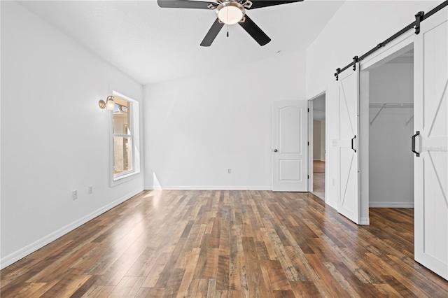 unfurnished bedroom with a walk in closet, a barn door, and hardwood / wood-style flooring