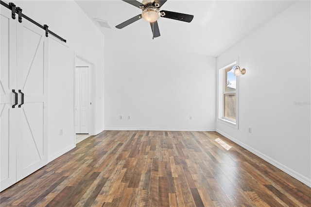 unfurnished bedroom with visible vents, baseboards, a barn door, and hardwood / wood-style flooring