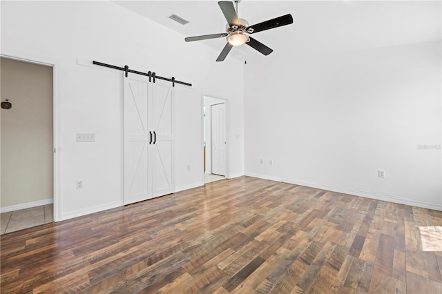 unfurnished bedroom with visible vents, a barn door, baseboards, and wood finished floors