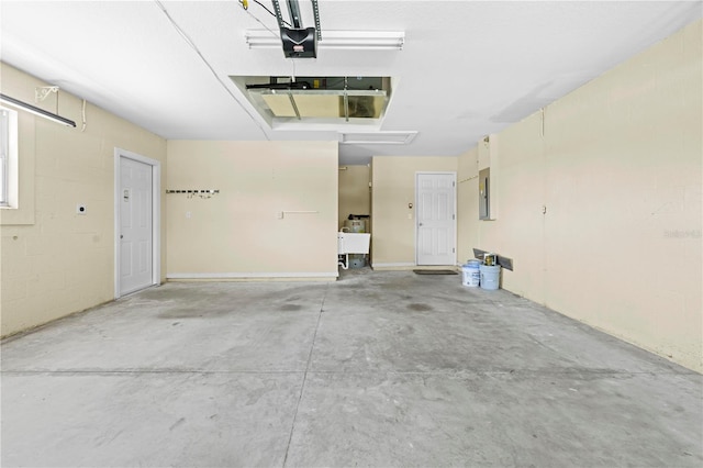 garage with electric panel, concrete block wall, a garage door opener, and a sink