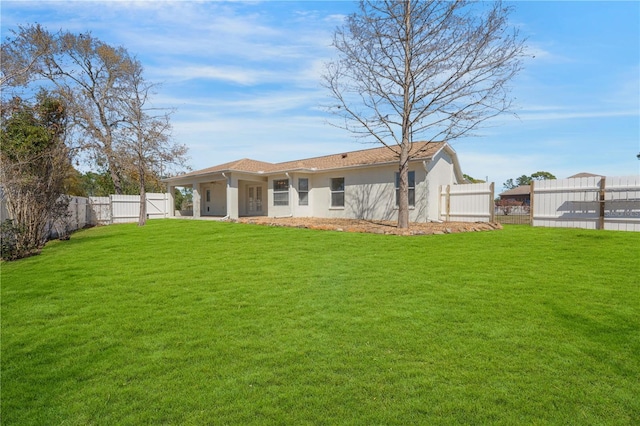 rear view of house featuring stucco siding, a lawn, a fenced backyard, and a gate