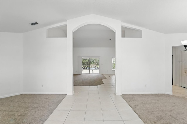 spare room featuring visible vents, light tile patterned flooring, arched walkways, vaulted ceiling, and light carpet