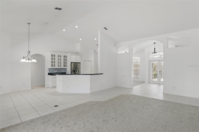 unfurnished living room featuring light colored carpet, light tile patterned floors, french doors, and arched walkways