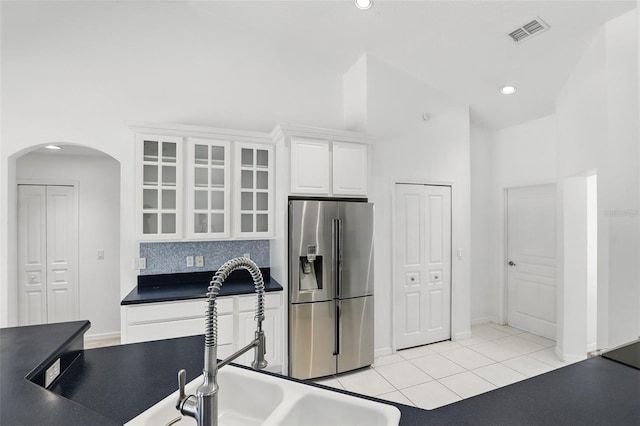 kitchen with visible vents, a sink, stainless steel fridge, arched walkways, and white cabinets