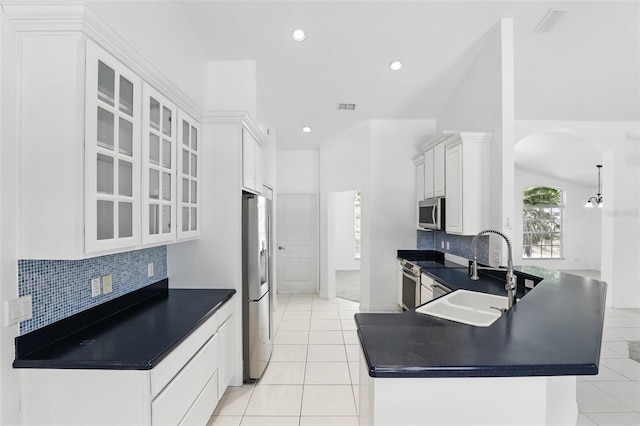 kitchen featuring a sink, stainless steel appliances, arched walkways, and dark countertops