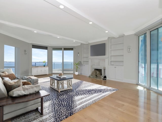 living room with built in shelves, crown molding, baseboards, a fireplace, and wood finished floors