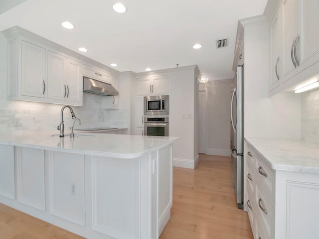 kitchen featuring visible vents, under cabinet range hood, a peninsula, stainless steel appliances, and white cabinetry