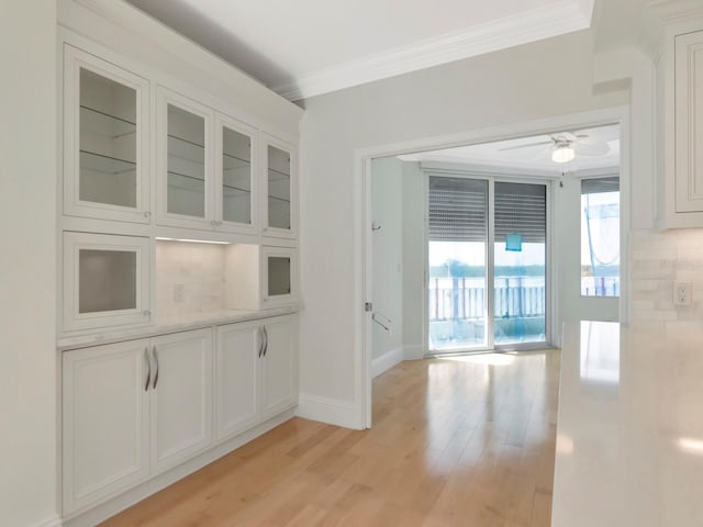 interior space featuring a ceiling fan, baseboards, light wood-style floors, and crown molding