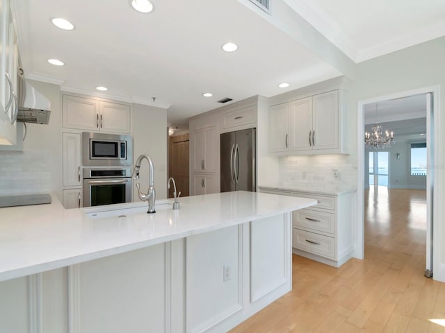 kitchen with light countertops, ornamental molding, appliances with stainless steel finishes, a peninsula, and light wood-style floors